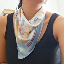 Load image into Gallery viewer, A woman wearing a black ribbed tank top and a light blue patterned neck scarf, looking upwards in a brightly lit indoor setting.